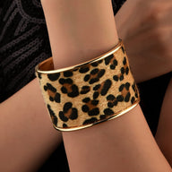 Bracelet manchette large en cuir imprimé léopard avec bordure dorée sur le poignet féminin.