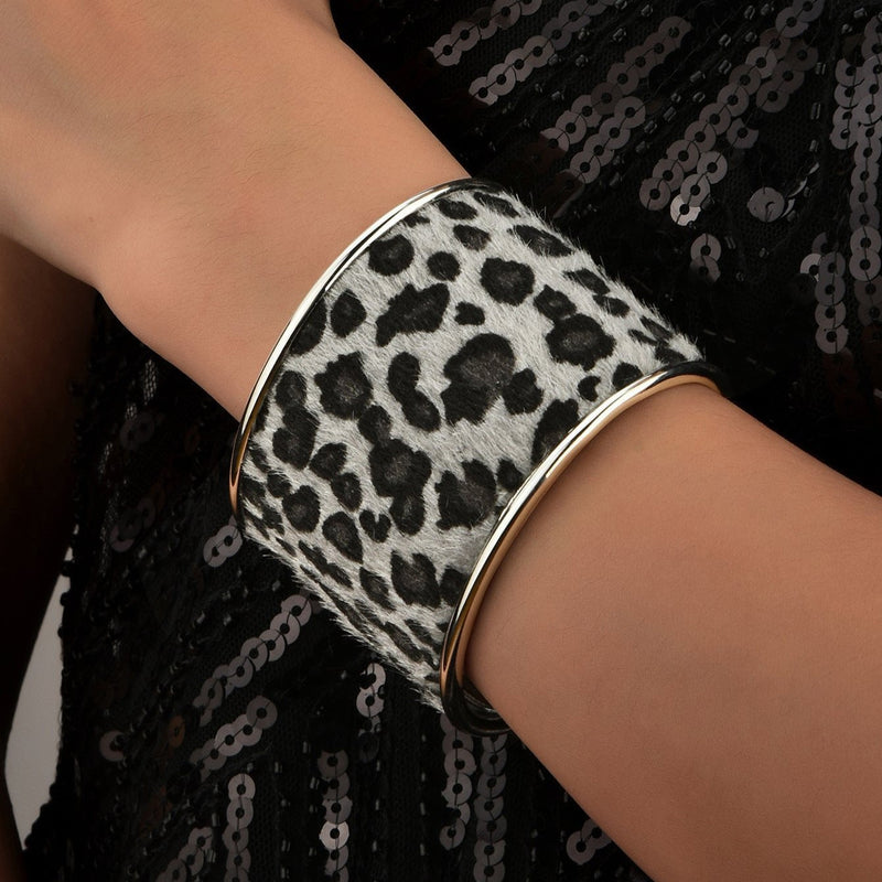 Bracelet manchette large effet léopard noir et blanc bordé d'argent porté au poignet féminin.