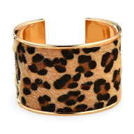 Bracelet manchette large en métal doré avec motif léopard texturé sur fond beige caramel.