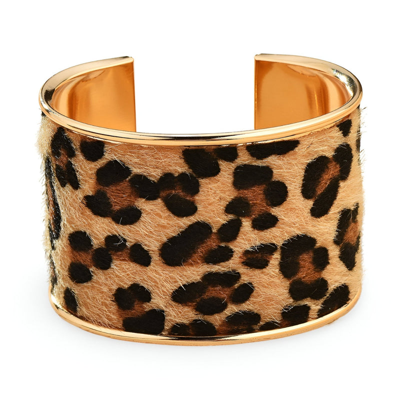 Bracelet manchette large en métal doré avec motif léopard texturé sur fond beige caramel.