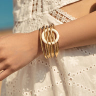 Bracelet manchette doré multi-anneaux avec fermoir circulaire sur poignet femme, style bohème chic.