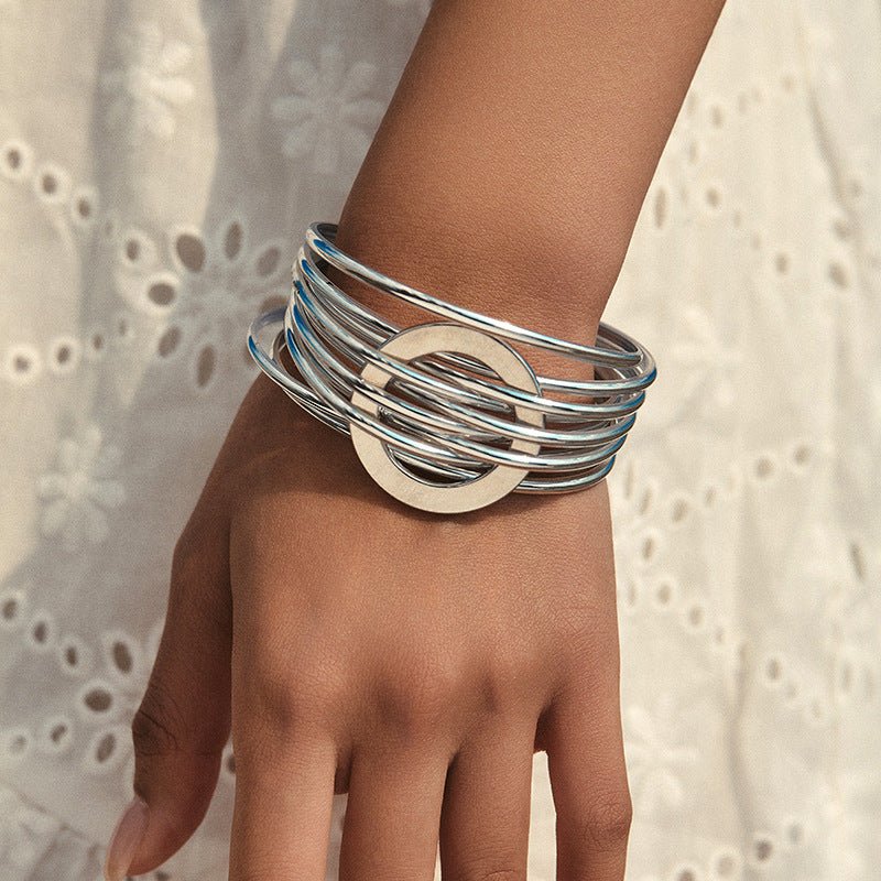 Bracelet manchette argenté multi-anneaux entrelacés avec cercle central lisse sur poignet féminin.