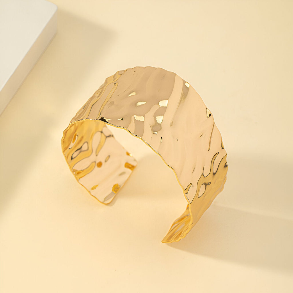 Bracelet manchette large en alliage métallique doré avec surface ondulée brillante.