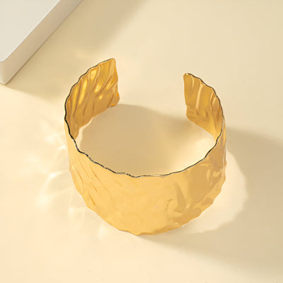 Bracelet manchette or ondulé en alliage métallique avec finition texturée brillante.