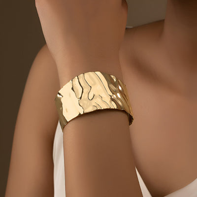 Bracelet manchette ondulé en alliage métallique doré, finition brillante et design texturé élégant.