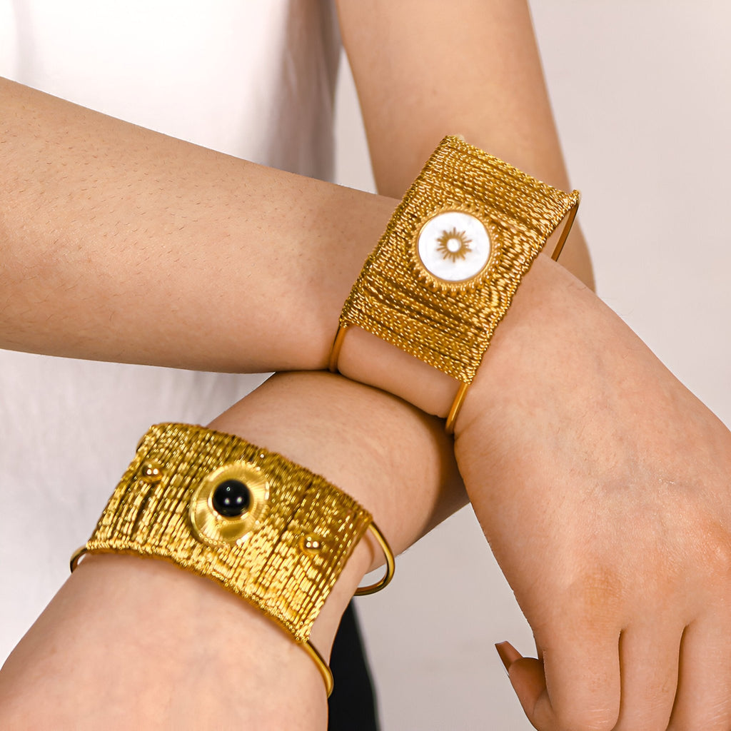 Bracelet manchette doré texturé avec pierre noire centrale sur poignet féminin.