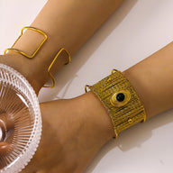 Bracelet manchette doré en métal texturé avec pierre noire ovale sertie, style moderne et élégant.