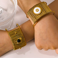 Bracelet manchette doré tissé avec pierre onyx noire centrale et détails métalliques fins.