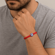 Bracelet fil rouge ciré avec un œil bleu et blanc, style minimaliste, porté au poignet homme.