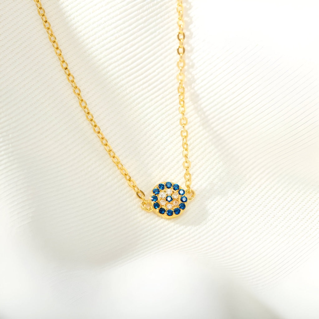 Bracelet en chaîne fine dorée avec pendentif rond orné de pierres bleues et blanches en forme d'œil.