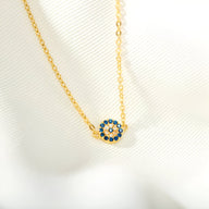 Bracelet en chaîne fine dorée avec pendentif rond orné de pierres bleues et blanches en forme d'œil.