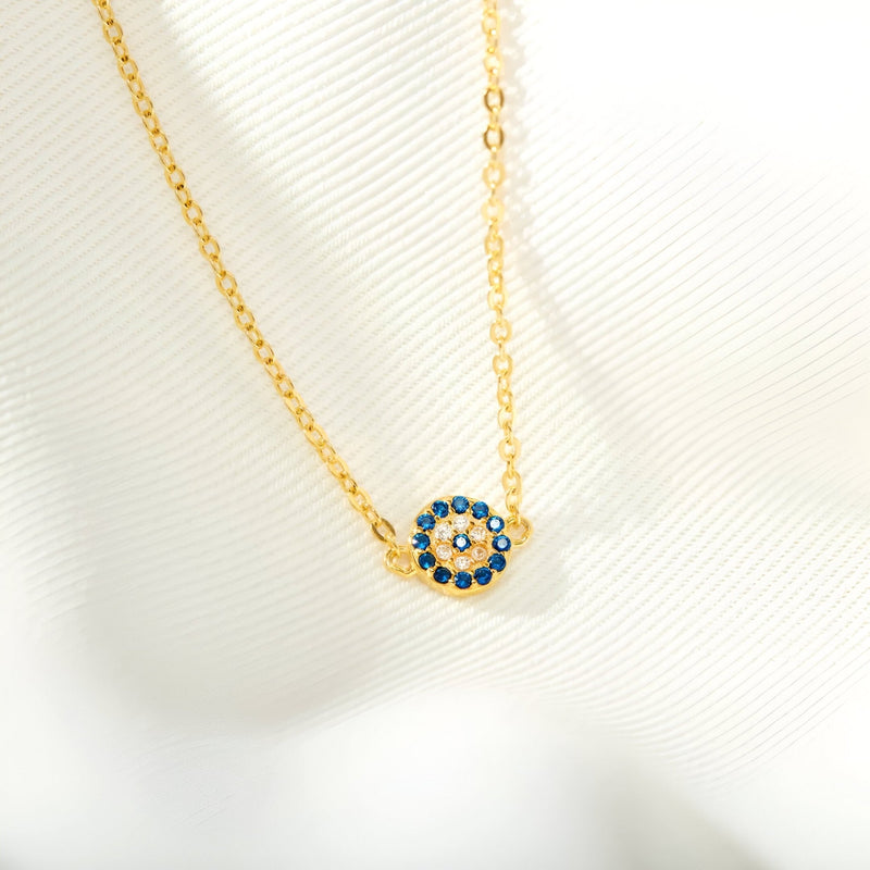 Bracelet en chaîne fine dorée avec pendentif rond orné de pierres bleues et blanches en forme d'œil.