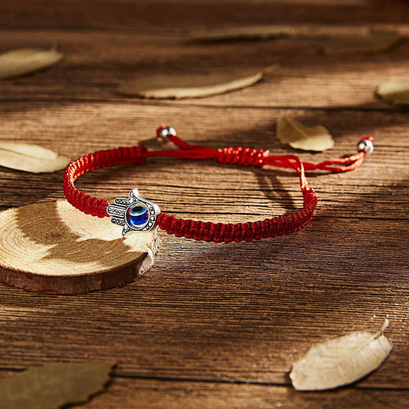Bracelet rouge en fil ciré avec pendentif œil bleu et main de Fatma argentée sur bois.