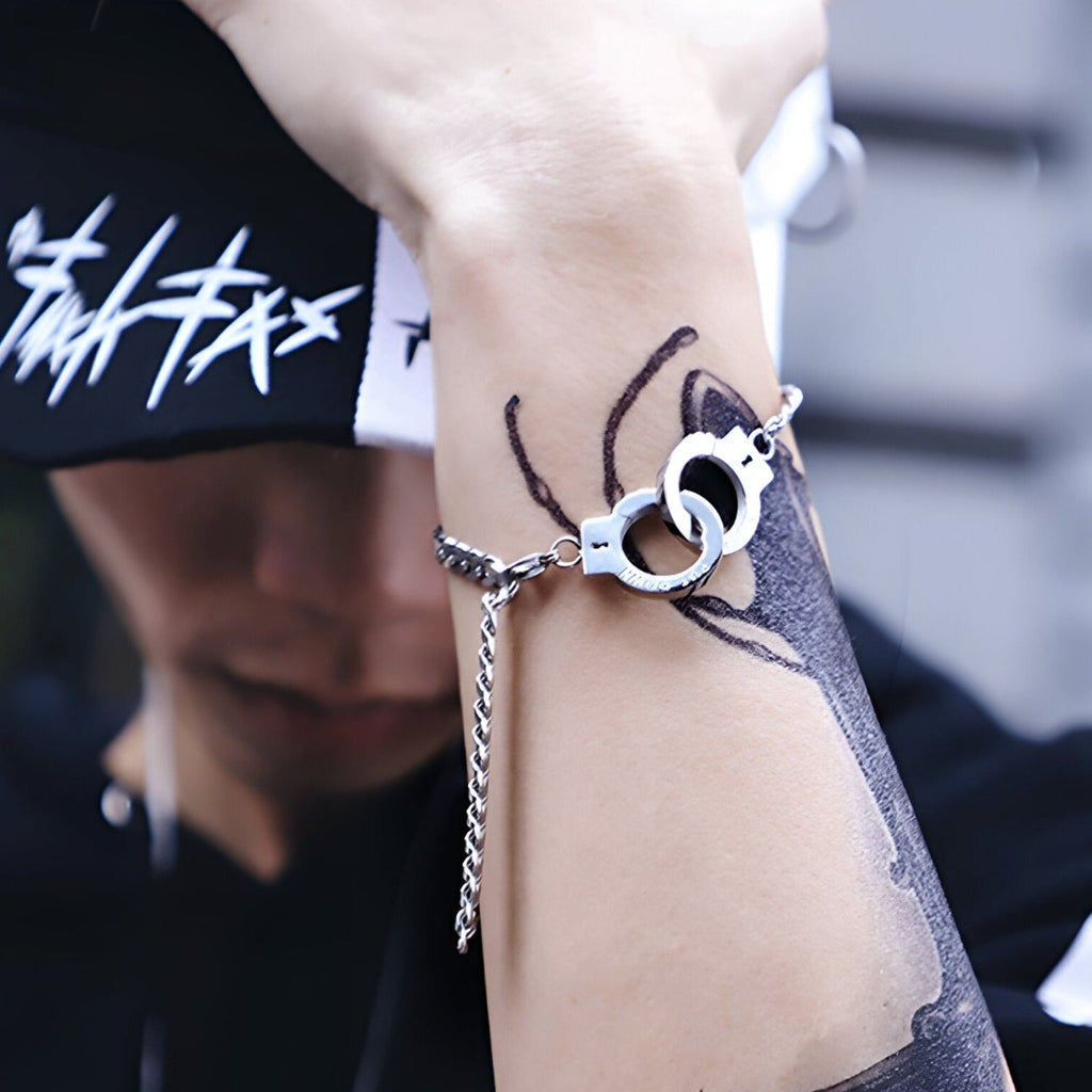 Bracelet menottes en acier inoxydable argenté avec chaîne fine porté au poignet.