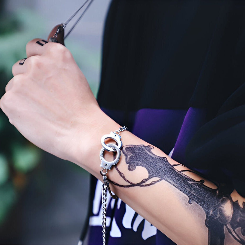 Bracelet menottes en acier inoxydable argenté autour du poignet avec chaîne fine.