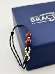 Bracelet noir en fil ciré avec trois pierres rouges de cinabre et un motif infini doré fin.