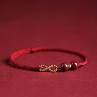 Bracelet minimaliste en fil ciré rouge avec pierres de cinabre bordeaux et motif infini doré.