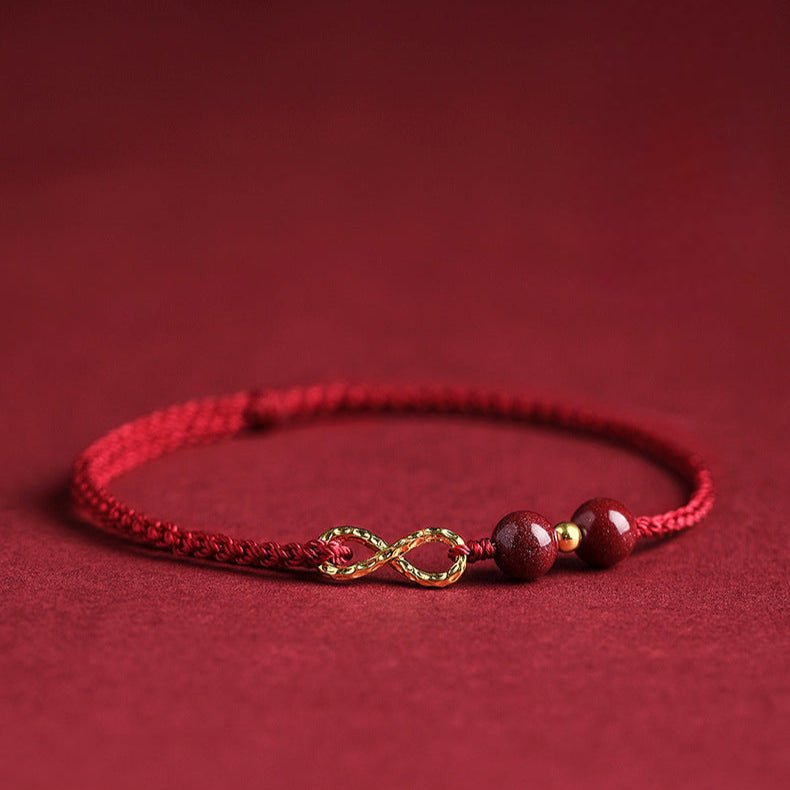 Bracelet minimaliste en fil ciré rouge avec pierres de cinabre bordeaux et motif infini doré.