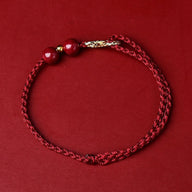 Bracelet fin en fil ciré bordeaux avec breloques en pierre de cinabre et motif infini doré.