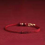 Bracelet fin rouge en fil ciré tressé avec motif infini en métal et petites perles de cinabre.