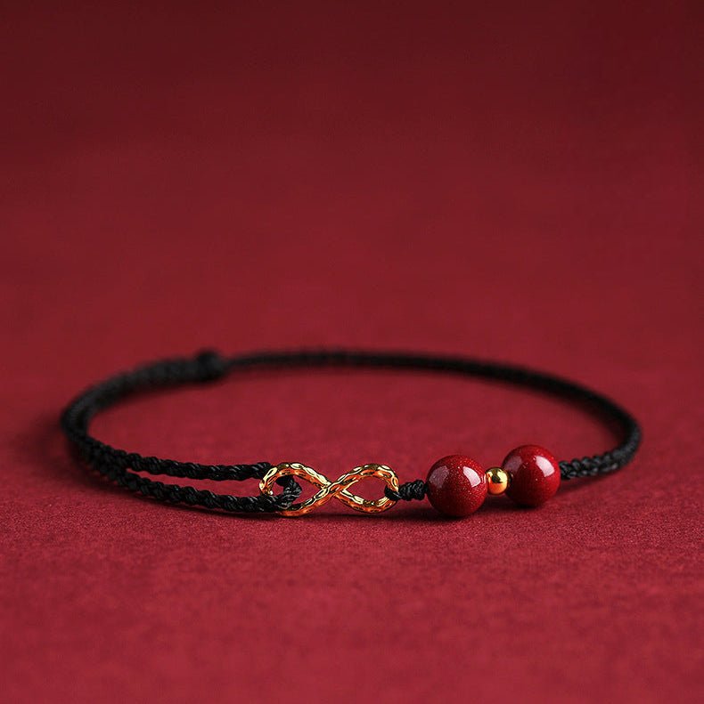 Bracelet noir en fil ciré avec motif infini doré et deux perles rouges de cinabre.