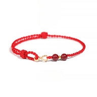 Bracelet minimaliste rouge en fil ciré avec motif infini doré et deux pierres de cinabre rondes.