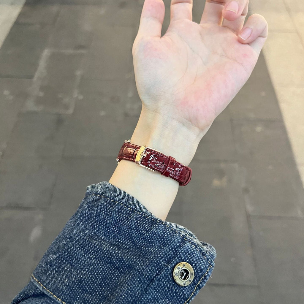 Bracelet montre effet crocodile rouge bordeaux en simili vegan avec boucle métallique dorée porté au poignet.