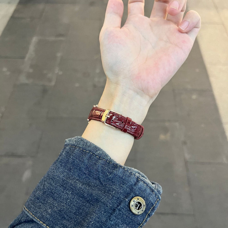 Bracelet montre effet crocodile rouge bordeaux en simili vegan avec boucle métallique dorée porté au poignet.