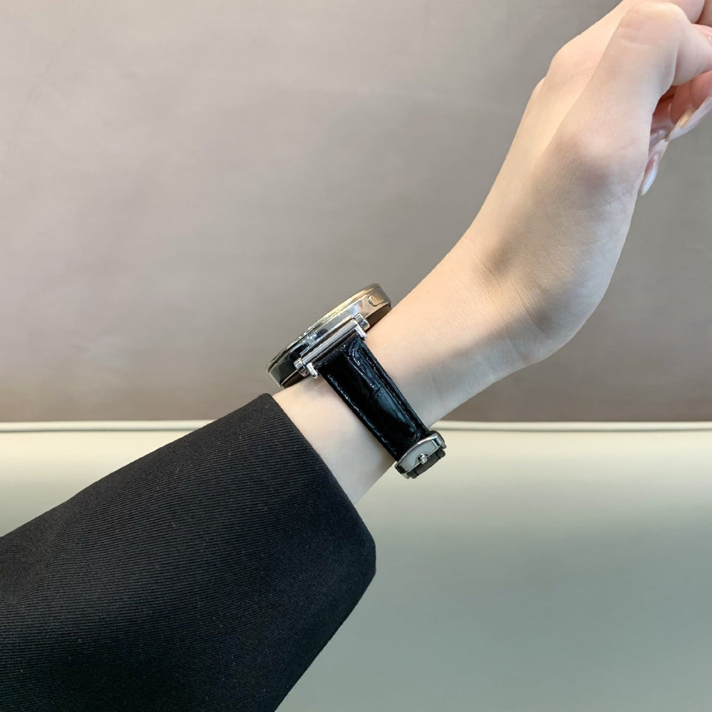 Bracelet montre noire effet crocodile en simili vegan avec boucle métal doré, porté au poignet féminin.