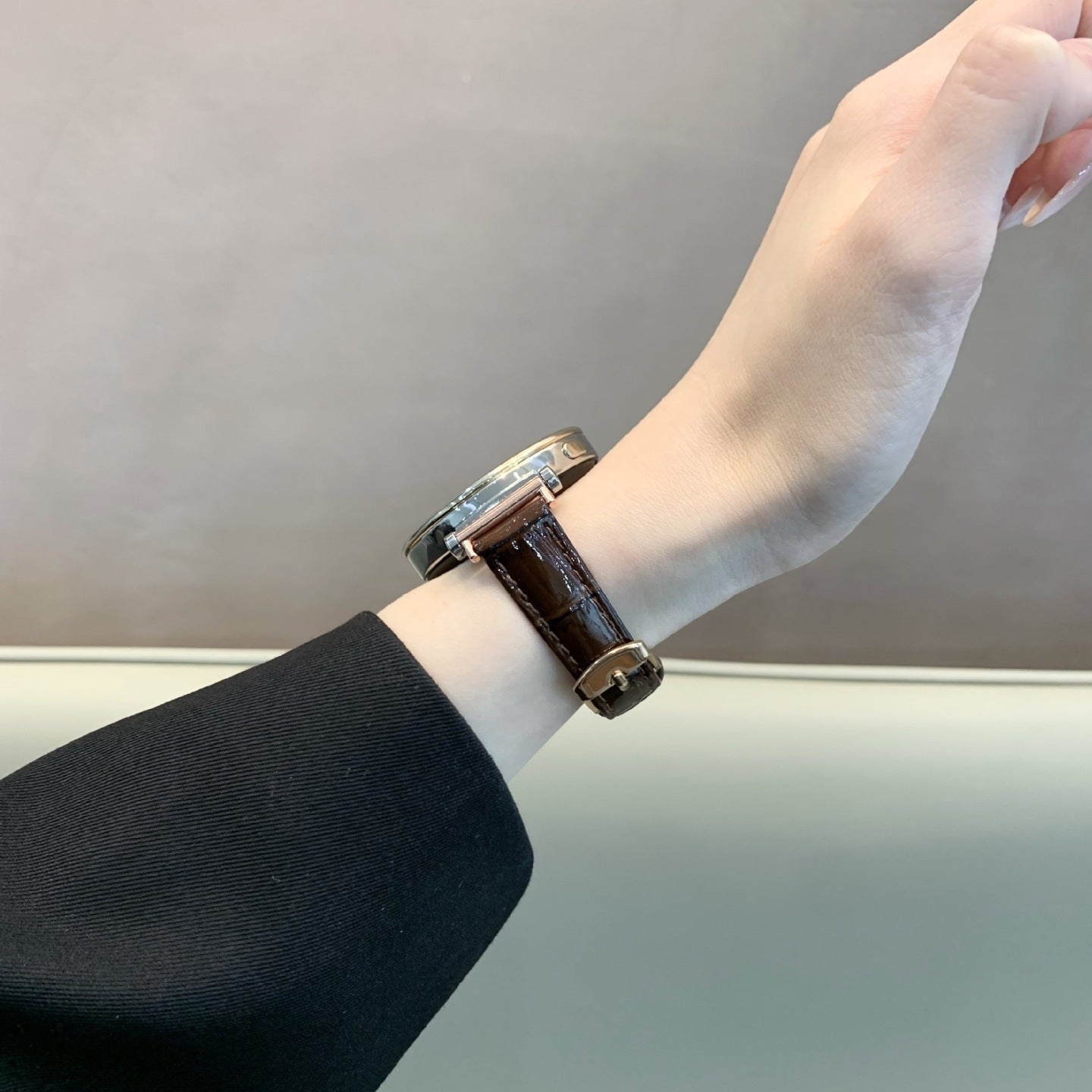 Bracelet montre simili cuir effet crocodile marron foncé avec boucle métal doré, porté au poignet féminin.