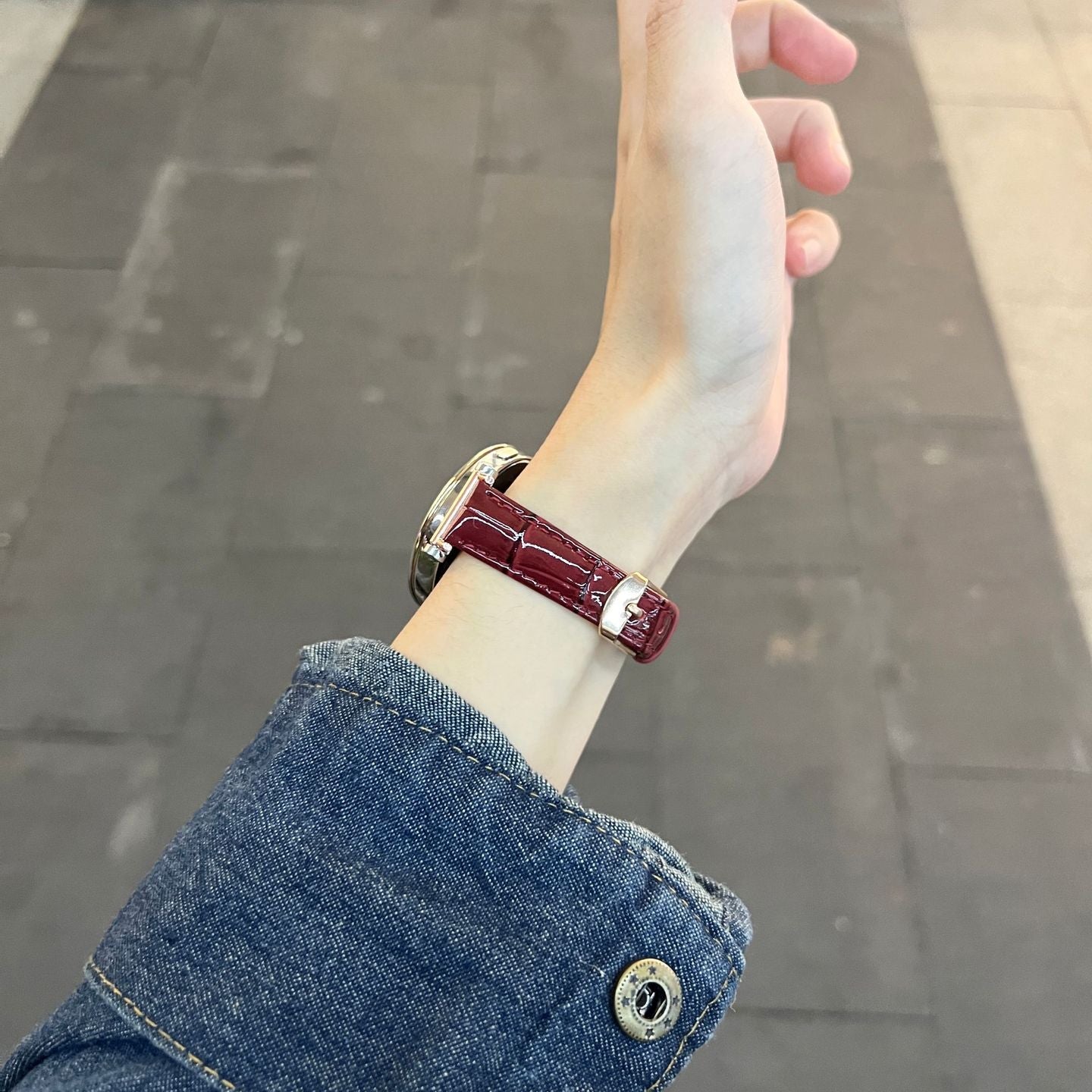 Bracelet montre connectée cuir simili effet crocodile rouge bordeaux avec boucle métal doré, porté sur poignet femme.