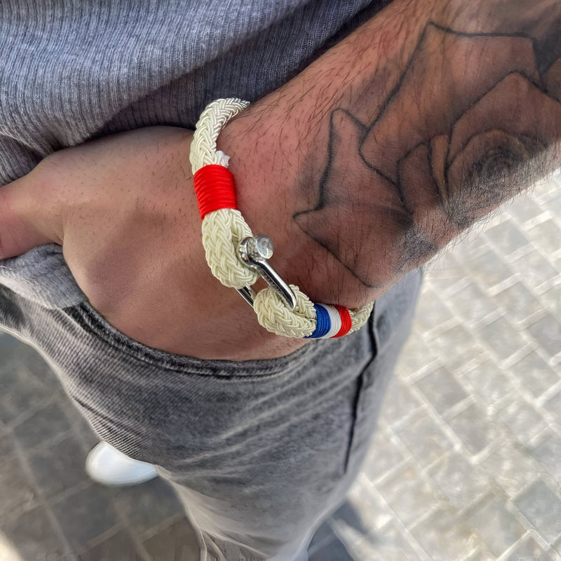 Bracelet mousqueton beige en coton avec détails drapeau français en acier inoxydable sur poignet tatoué.