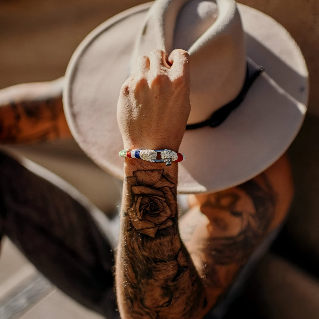 Bracelet mousqueton beige en coton et acier avec drapeau français porté au poignet d’un homme tatoué.