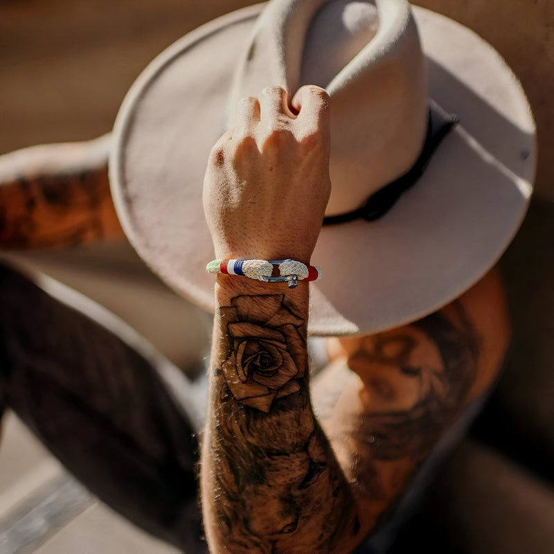 Bracelet mousqueton beige en coton et acier avec drapeau français porté au poignet d’un homme tatoué.