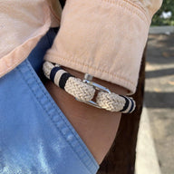 Bracelet beige tressé en coton avec mousqueton en acier inoxydable sur poignet homme.