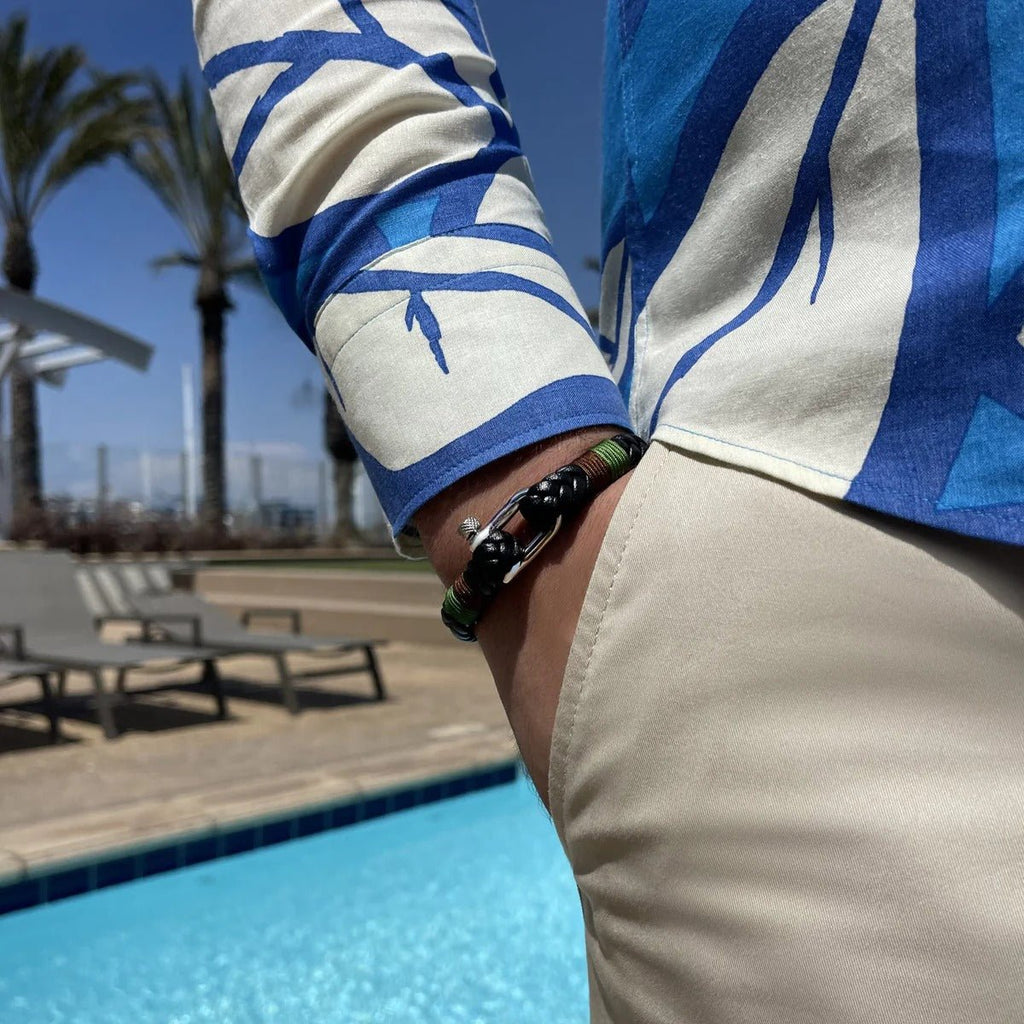 Bracelet mousqueton en cuir noir, vert et marron avec acier inoxydable porté au poignet d’un homme au bord d’une piscine.