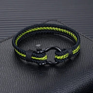 Bracelet triple cordon noir et vert avec mousqueton en acier inoxydable sur fond texturé noir.