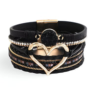 Bracelet multi-rangs noir avec grand cœur doré et détails en strass et cuir tressé.