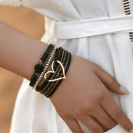 Bracelet multi-rangs noir avec grand cœur central doré et détails de perles fines sur poignet féminin.