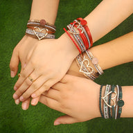 Bracelets multi-rangs en cuir et perles, grand cœur métallique central, couleurs variées sur poignets féminins.