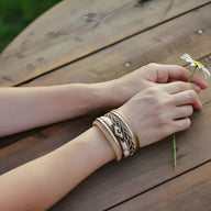 Bracelet multi-rangs beige avec perles et détails tressés porté au poignet féminin.