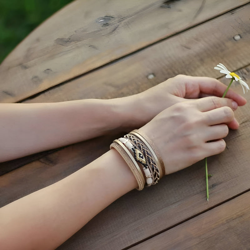 Bracelet multi-rangs beige avec perles et détails tressés porté au poignet féminin.