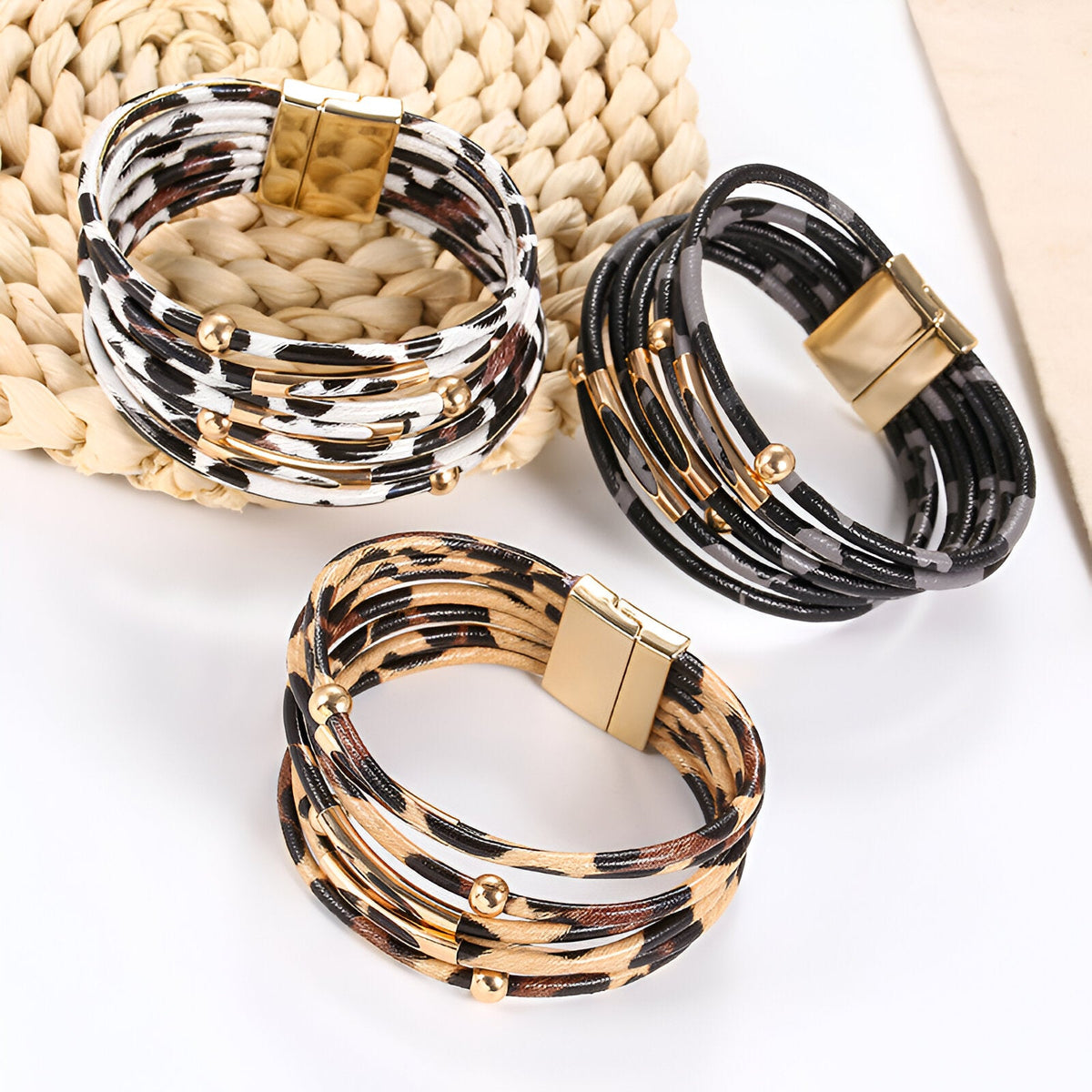 Trois bracelets multi-rangs léopard en cuir beige, noir et blanc avec fermoirs dorés.