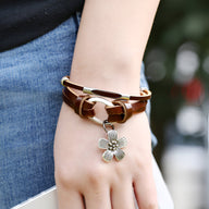 Bracelet multi-rangs en cuir marron avec charm fleur en métal argenté porté au poignet.