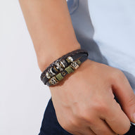 Bracelet multi-rangs marron en cuir et bois avec ornement croix métal porté au poignet.