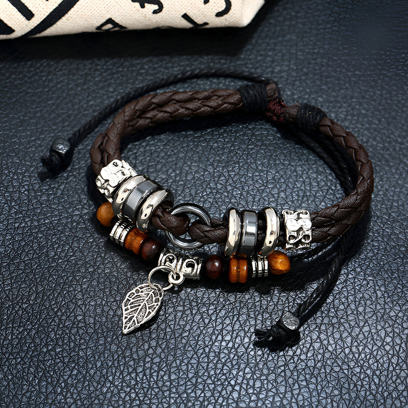 Bracelet multi-rangs en cuir marron tressé avec perles en bois, anneaux métalliques et pendentif feuille argenté pour homme.