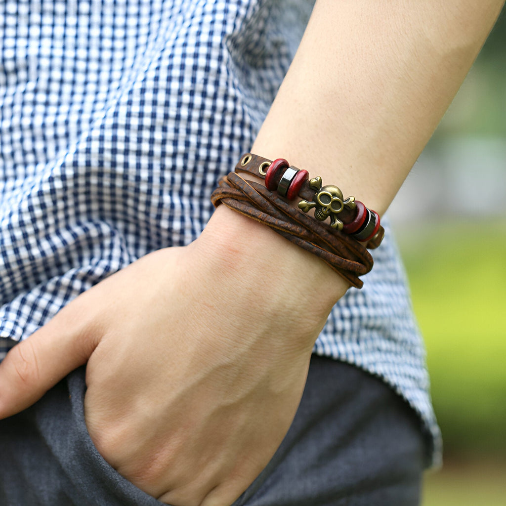 Bracelet multi-rangs en cuir marron avec tête de mort en métal et perles rouges et blanches.