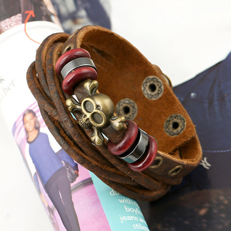 Bracelet multi-rangs en cuir marron avec tête de mort métal doré et perles rouges et noires, fermoir à boutons-pression.