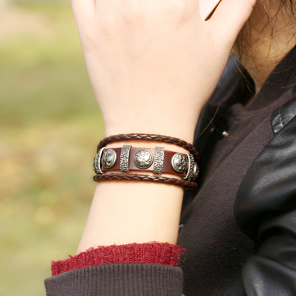 Bracelet multi-rangs en cuir marron avec têtes de mort métalliques et lanière tressée.