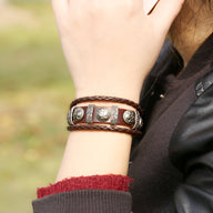 Bracelet multi-rangs en cuir marron avec têtes de mort métalliques et lanière tressée.